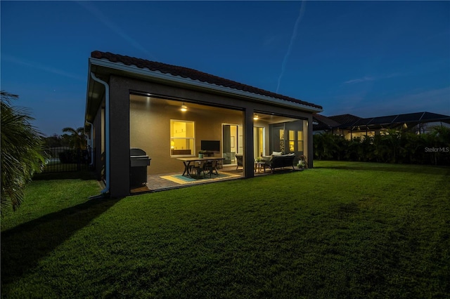 back house at dusk featuring a patio area and a yard