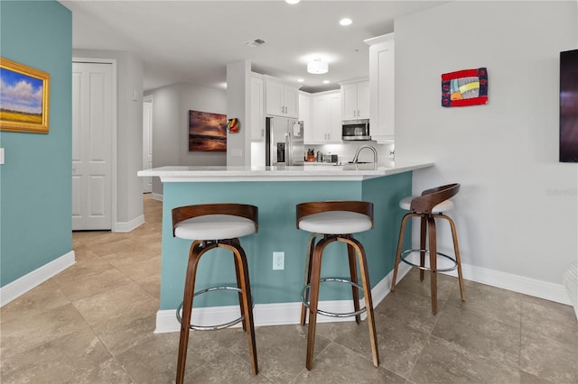 kitchen featuring white cabinetry, sink, stainless steel appliances, a kitchen breakfast bar, and kitchen peninsula