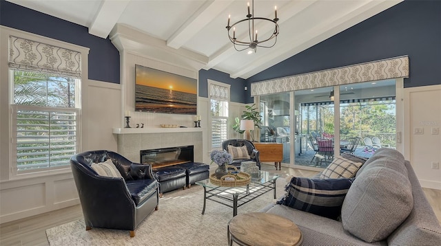 living room with a tile fireplace, lofted ceiling with beams, ceiling fan with notable chandelier, and light hardwood / wood-style floors