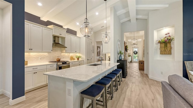 kitchen featuring pendant lighting, wall chimney range hood, sink, gas range, and light stone counters