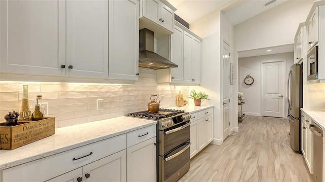 kitchen featuring stainless steel appliances, light stone counters, white cabinetry, and wall chimney range hood