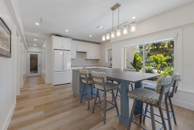 kitchen with hanging light fixtures, light hardwood / wood-style flooring, white fridge, a breakfast bar, and white cabinets