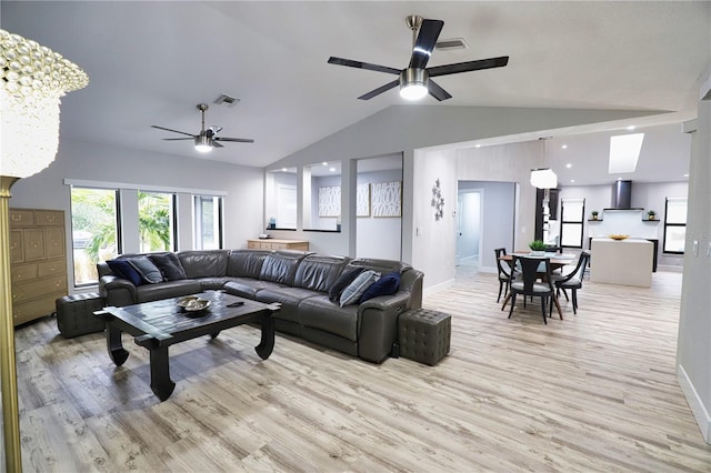 living room with ceiling fan with notable chandelier, light hardwood / wood-style floors, and lofted ceiling with skylight