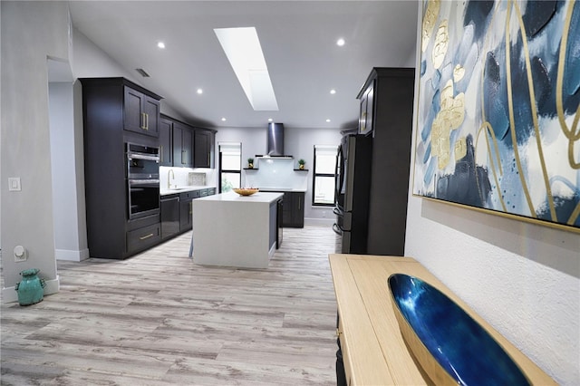 kitchen with sink, a skylight, wall chimney exhaust hood, fridge, and a kitchen island