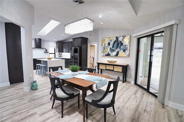 dining space featuring lofted ceiling with skylight, light hardwood / wood-style flooring, and an inviting chandelier