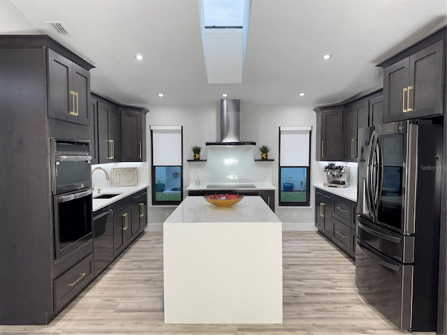 kitchen with a center island, black appliances, wall chimney range hood, a skylight, and tasteful backsplash