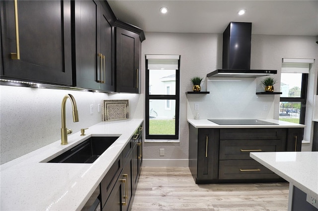 kitchen featuring sink, wall chimney exhaust hood, black electric cooktop, light hardwood / wood-style floors, and light stone counters