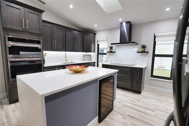 kitchen featuring stainless steel double oven, beverage cooler, sink, wall chimney range hood, and lofted ceiling