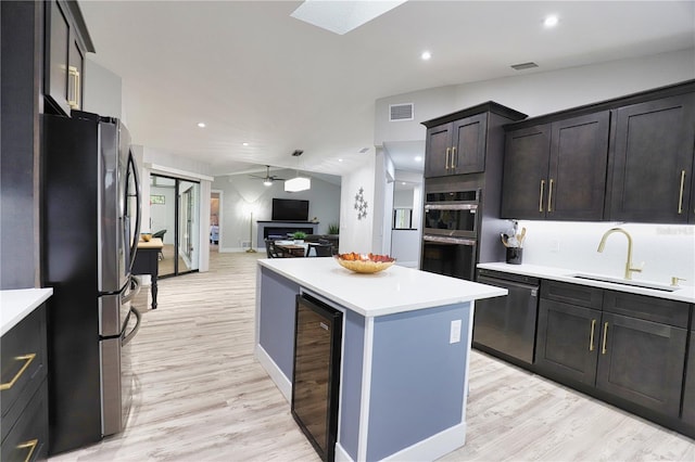 kitchen featuring a center island, sink, ceiling fan, appliances with stainless steel finishes, and beverage cooler