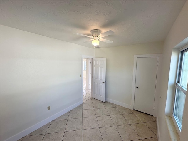 empty room with a textured ceiling, ceiling fan, and light tile patterned flooring