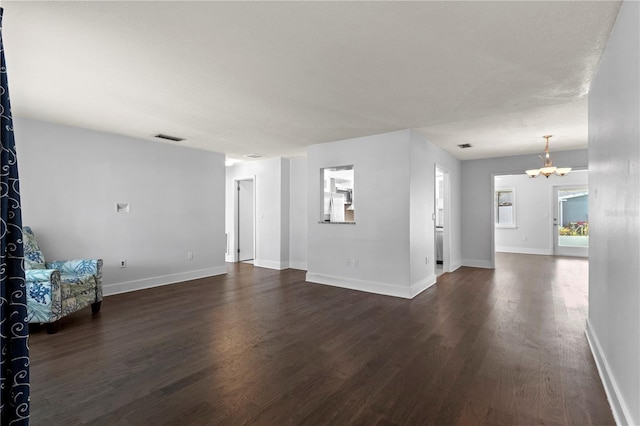 unfurnished living room featuring visible vents, baseboards, a chandelier, and dark wood finished floors