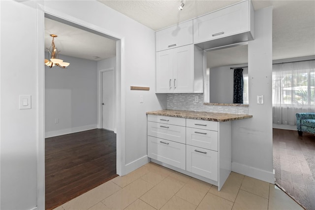kitchen with white cabinets, light wood-style floors, baseboards, decorative backsplash, and a chandelier