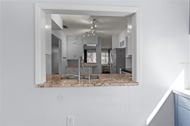 kitchen with light stone counters, visible vents, a sink, freestanding refrigerator, and a textured ceiling