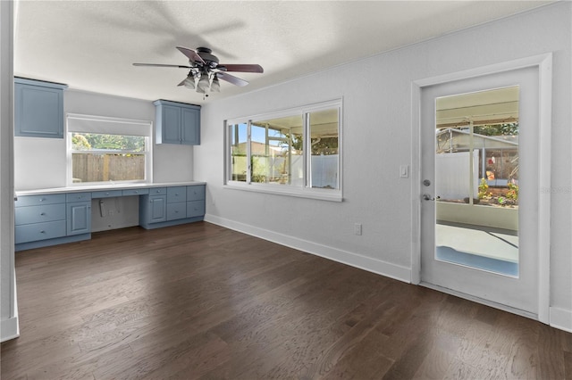 unfurnished office with baseboards, a ceiling fan, built in desk, and dark wood finished floors
