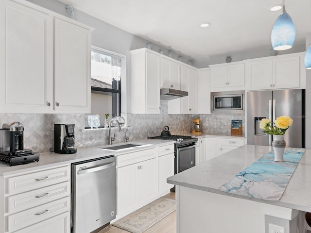 kitchen with sink, decorative light fixtures, decorative backsplash, appliances with stainless steel finishes, and light wood-type flooring