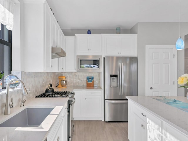 kitchen with white cabinets, sink, range hood, light stone counters, and stainless steel appliances