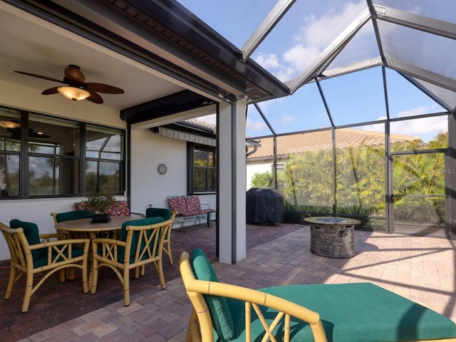 view of patio featuring area for grilling, ceiling fan, glass enclosure, and a fire pit