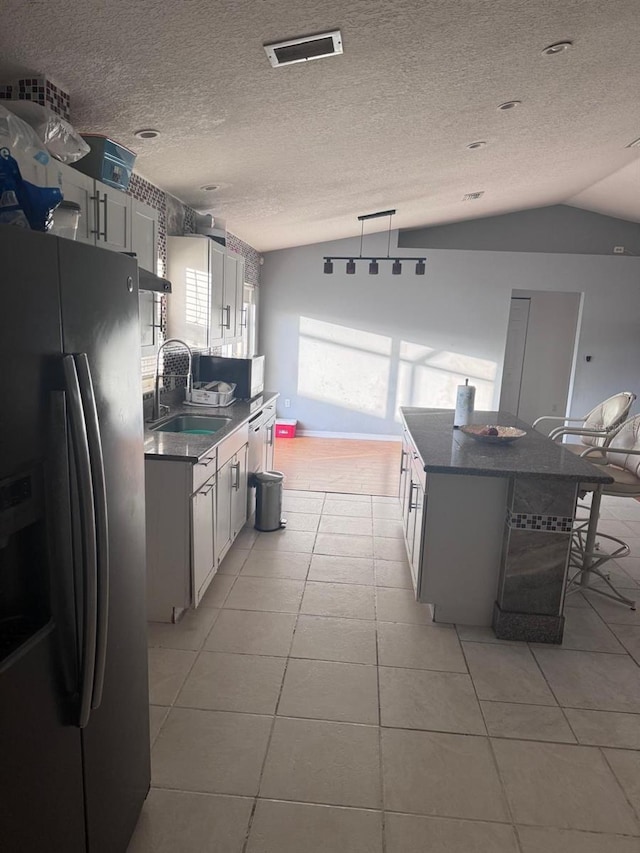 kitchen featuring white cabinets, stainless steel fridge with ice dispenser, vaulted ceiling, and sink