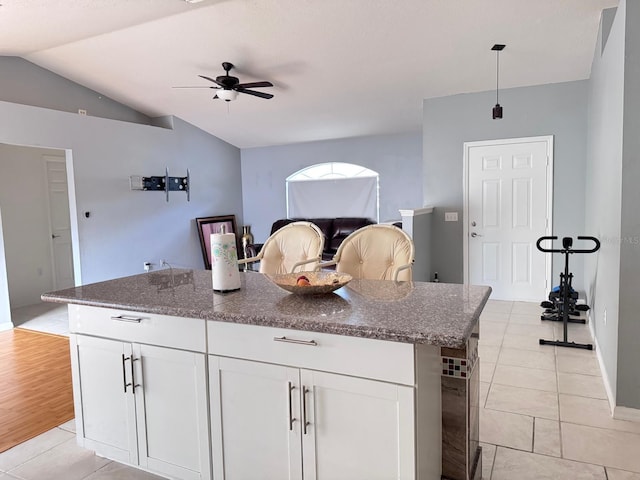 kitchen featuring a center island, vaulted ceiling, dark stone countertops, light hardwood / wood-style floors, and white cabinetry