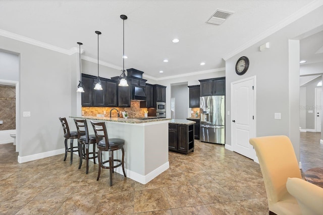 kitchen featuring light stone counters, stainless steel appliances, a center island with sink, hanging light fixtures, and a breakfast bar area