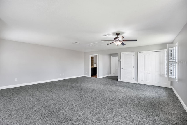 unfurnished bedroom with ceiling fan, ensuite bathroom, two closets, and dark colored carpet