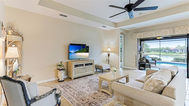 living room featuring a raised ceiling, ceiling fan, and light tile patterned floors