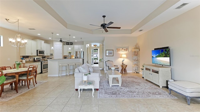 tiled living room featuring a raised ceiling and ceiling fan with notable chandelier