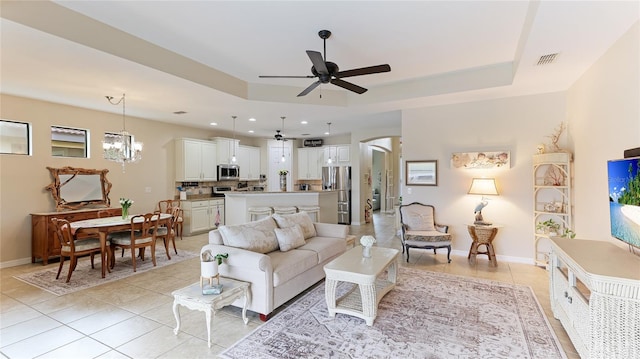 living room featuring light tile patterned floors, ceiling fan with notable chandelier, and a tray ceiling