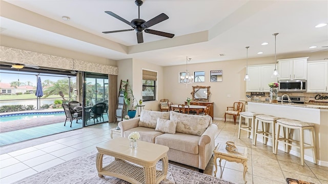 tiled living room with a tray ceiling and ceiling fan with notable chandelier