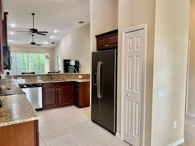 kitchen featuring lofted ceiling, sink, light tile patterned floors, appliances with stainless steel finishes, and light stone counters