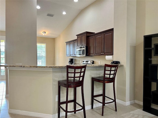 kitchen with a breakfast bar, kitchen peninsula, light stone countertops, light tile patterned floors, and dark brown cabinetry