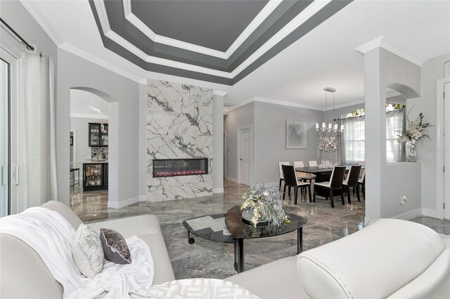 living room featuring a tray ceiling, crown molding, a fireplace, and an inviting chandelier