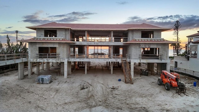 back of house at dusk featuring a carport, stairway, and a balcony