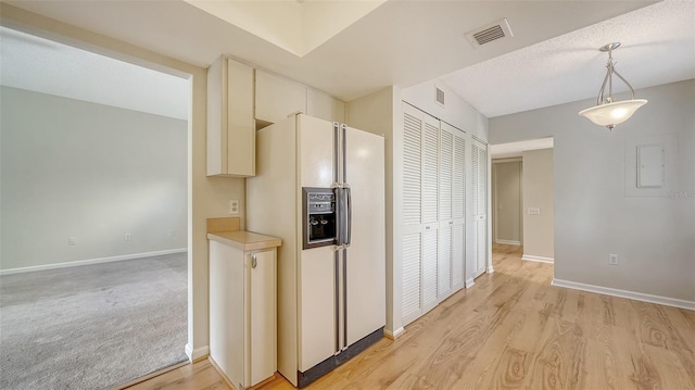 kitchen featuring decorative light fixtures, light wood-type flooring, white fridge with ice dispenser, and a textured ceiling