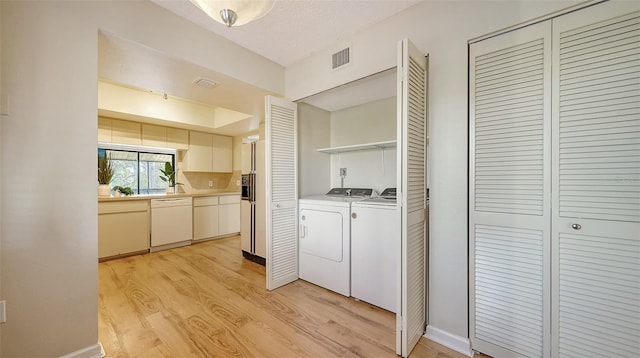 clothes washing area featuring washer and clothes dryer, light hardwood / wood-style floors, and a textured ceiling