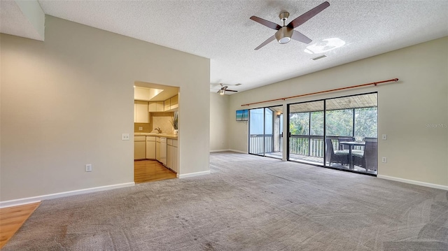 unfurnished living room with ceiling fan, light colored carpet, and a textured ceiling