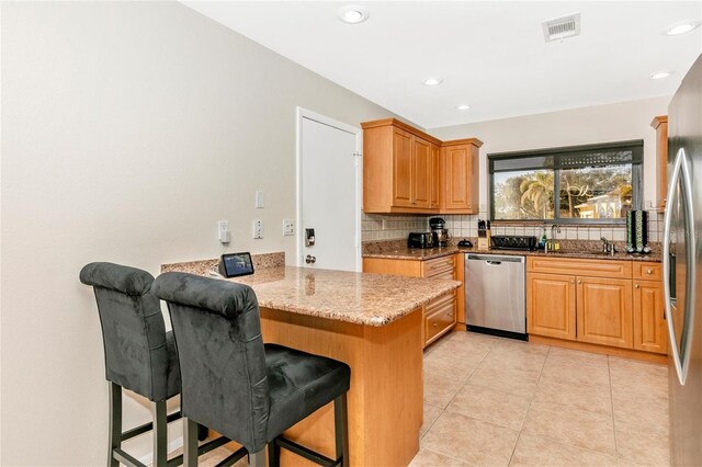 kitchen featuring stainless steel dishwasher, light stone countertops, a kitchen bar, and kitchen peninsula