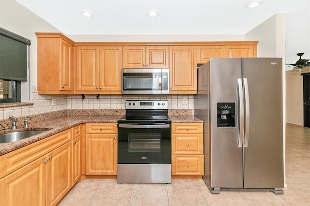 kitchen with tasteful backsplash, appliances with stainless steel finishes, light tile patterned flooring, a sink, and dark stone countertops