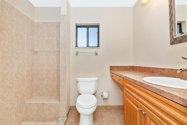 bathroom featuring toilet, vanity, tile patterned flooring, tiled shower, and baseboards