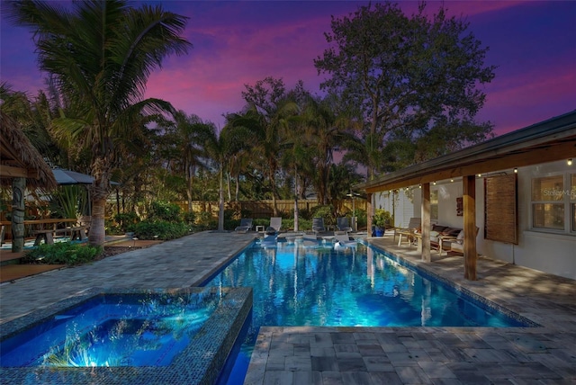 pool at dusk with a patio and a hot tub