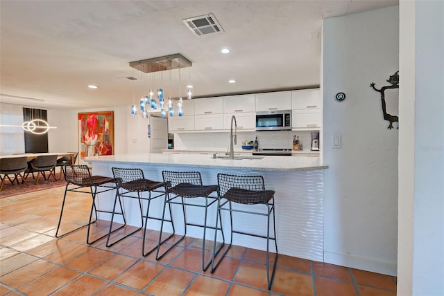 kitchen with white cabinetry, sink, light stone counters, pendant lighting, and a breakfast bar area