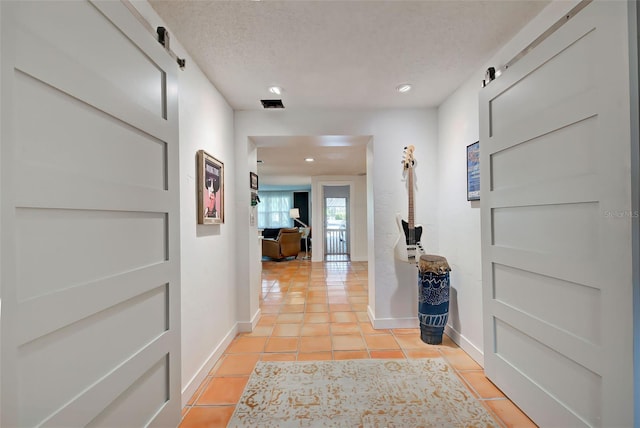 hallway with a barn door, light tile patterned flooring, and a textured ceiling