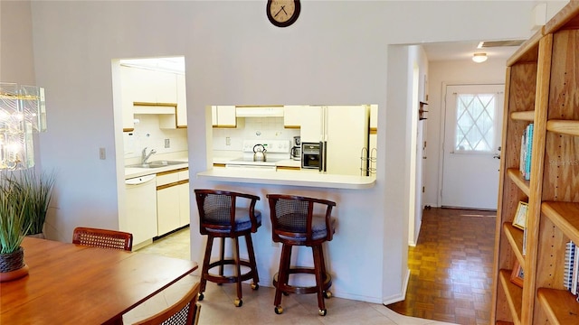 kitchen with white appliances, white cabinets, sink, kitchen peninsula, and light parquet flooring