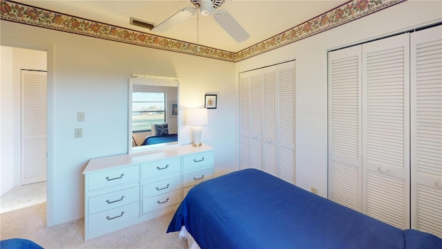 bedroom with light carpet, ceiling fan, and multiple closets