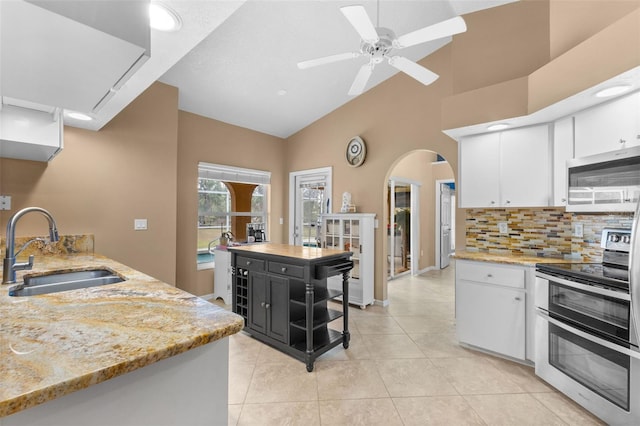 kitchen with sink, stainless steel appliances, light stone counters, lofted ceiling, and white cabinets