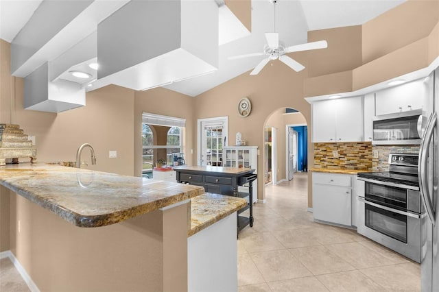 kitchen featuring kitchen peninsula, light tile patterned floors, light stone countertops, appliances with stainless steel finishes, and white cabinetry