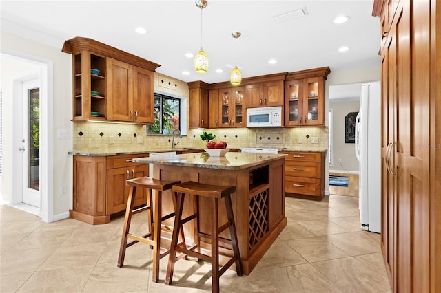 kitchen featuring light stone countertops, tasteful backsplash, decorative light fixtures, white appliances, and a kitchen island