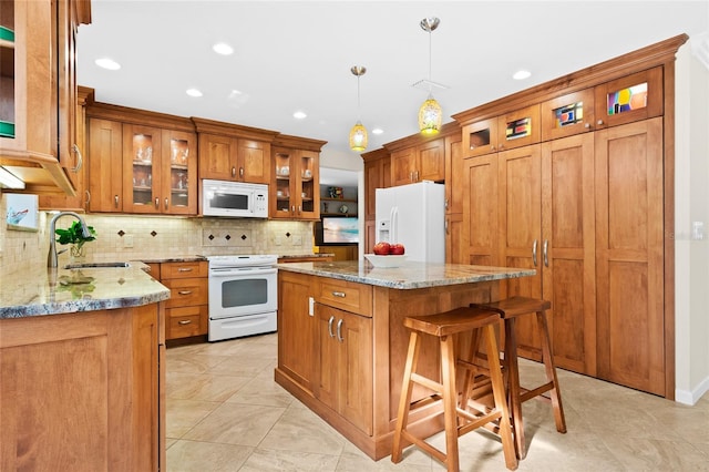 kitchen featuring light stone counters, white appliances, sink, decorative light fixtures, and a center island