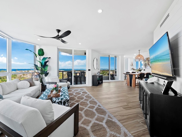 living room featuring ceiling fan, a wall of windows, and light wood-type flooring