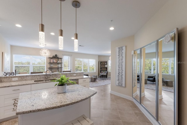 kitchen with light stone countertops, a center island, sink, hanging light fixtures, and white cabinets